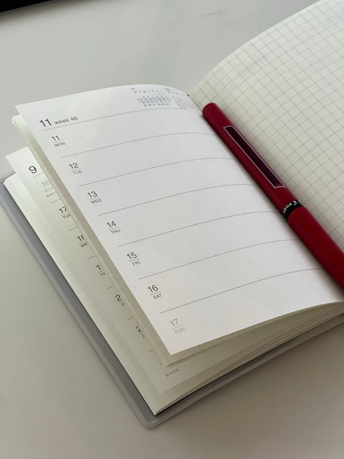 An open planner and red pen on a desk, ideal for office or study settings.